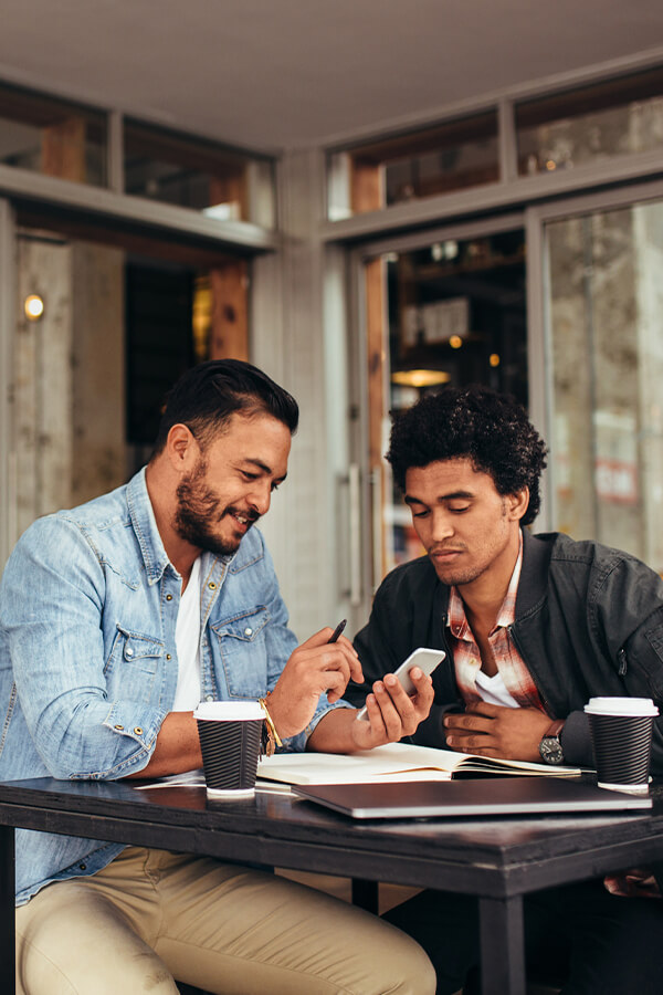 Two men sitting at a cafe looking at a phone
