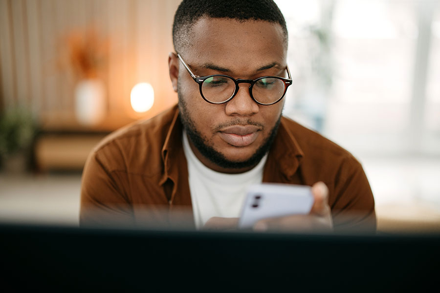 Man looking at phone while sitting in front of computer.